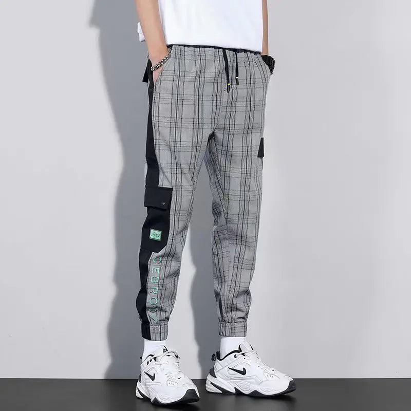 Person wearing gray checkered pants with black accents and white sneakers on a plain background